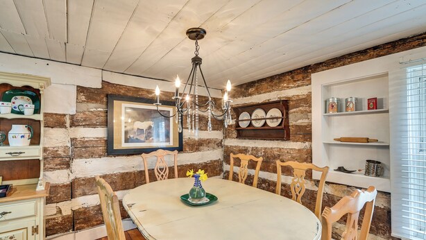 A dining area with a round table, wooden chairs, a chandelier, and rustic brick walls. - Georgetown Home Near Kentucky Horse Park! (Georgetown)