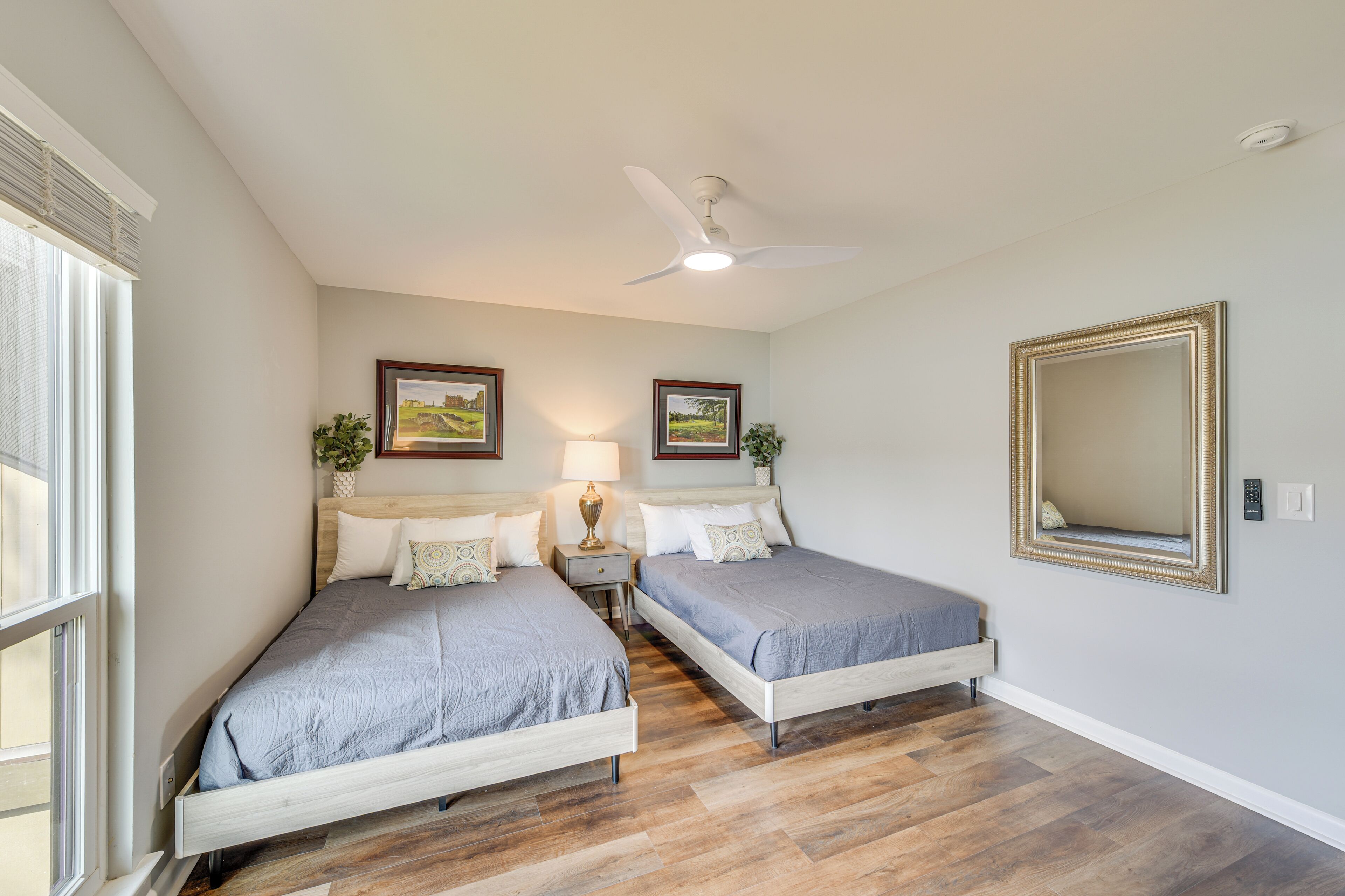 Ein Schlafzimmer mit zwei Einzelbetten, einem Deckenventilator, einem großen Spiegel und gerahmten Bildern an der Wand.