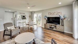 A spacious living room with a dining area, a kitchen in the background, and a balcony. - Pinehurst Lake Condo: Water View & Community Perks (Pinehurst)