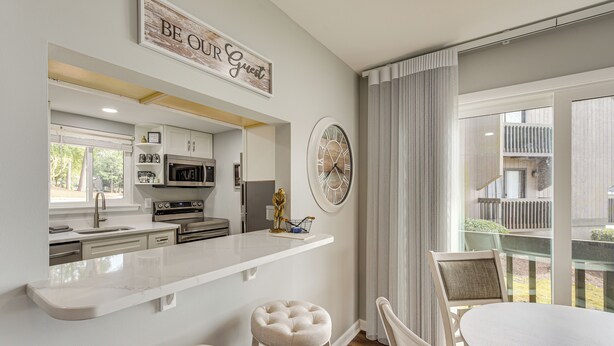 A modern kitchen with a central island, bar stools, and a dining table with chairs. - Pinehurst Lake Condo: Water View & Community Perks (Pinehurst)
