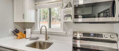 A modern kitchen with white cabinets, a stainless steel sink, a built-in microwave, and an oven.