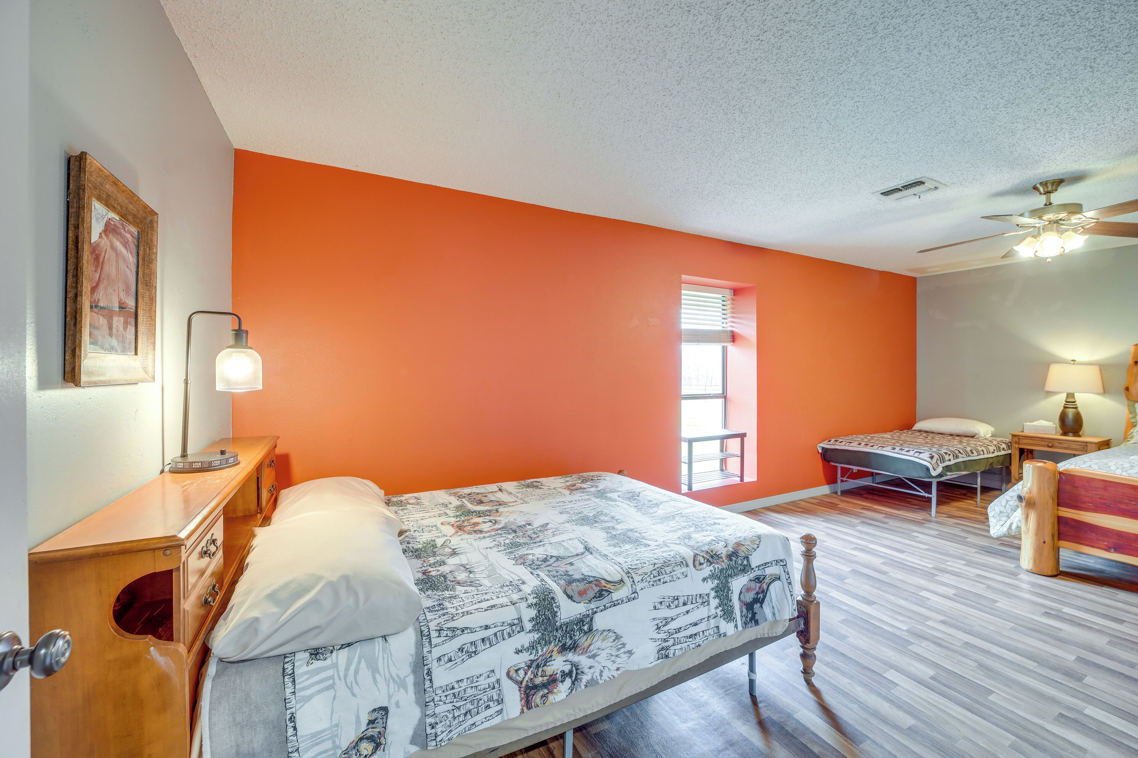 Une chambre à coucher comprenant un lit, une table de chevet, une commode, une fenêtre avec des stores et un ventilateur de plafond.