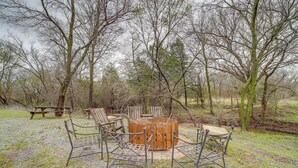 A rustic outdoor seating area with a circular wooden table surrounded by metal chairs, set on a gravel surface with trees in the background. - Outdoorsy Getaway Near Atoka: Hunt, Fish & Relax! (Pittsburg)
