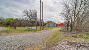 A gravel driveway leading to a green house with a sign welcoming visitors to Hard Wood Outdoors. - Outdoorsy Getaway Near Atoka: Hunt, Fish & Relax! (Pittsburg)