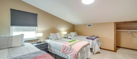 A bedroom with two beds, a window with blinds, a bedside table with a lamp, and a closet with a hanging rod.