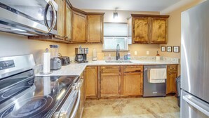 A kitchen with wooden cabinets, stainless steel appliances, a granite countertop, and a window with blinds.