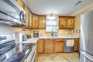 A kitchen with wooden cabinets, stainless steel appliances, a granite countertop, and a window with blinds.
