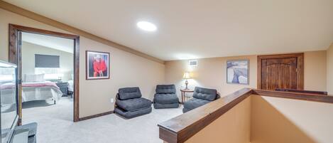 A spacious room with a large bed, a desk, and a chair. There is a window with blinds, a lamp, and a framed picture on the wall.