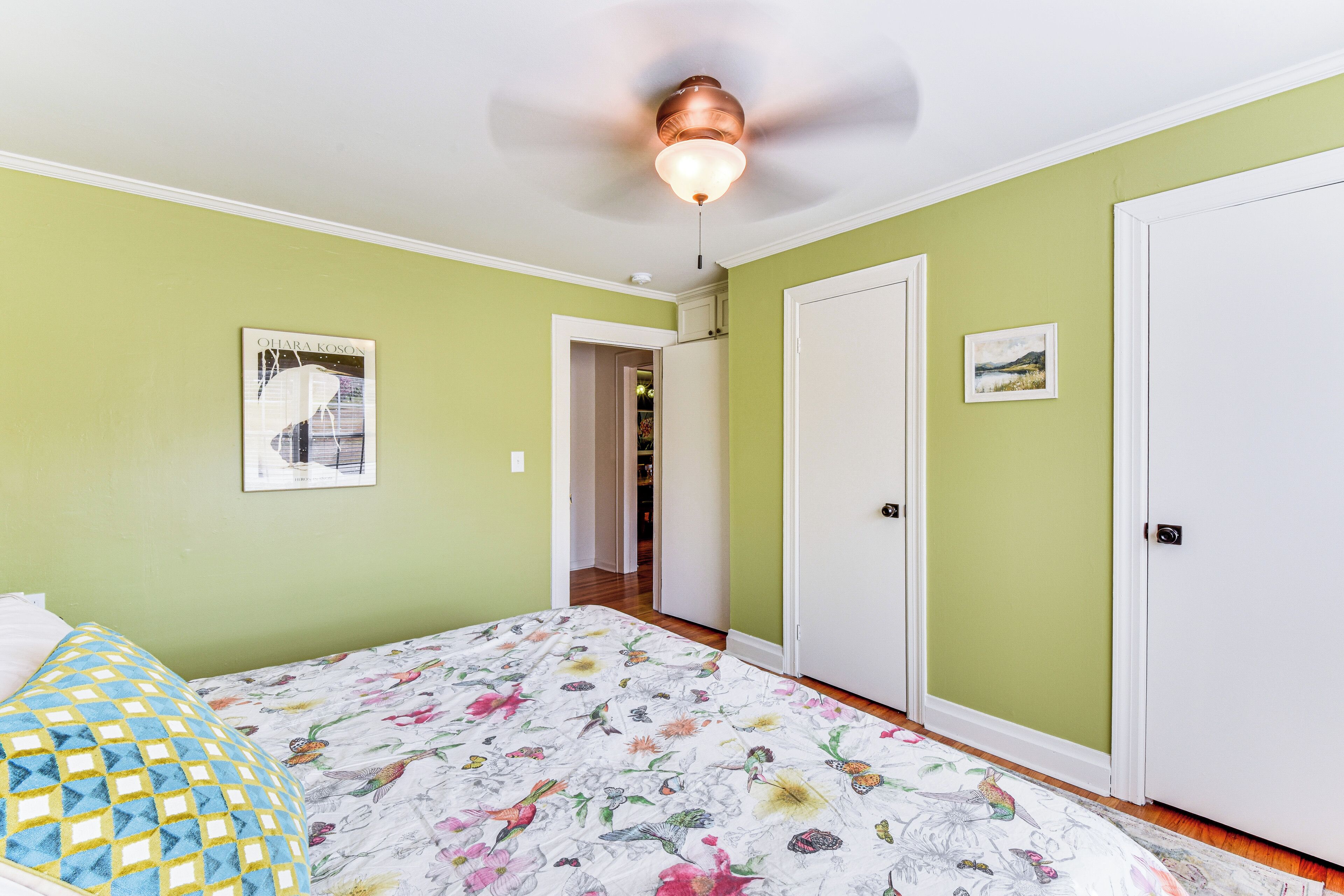 A bedroom with a floral bedspread, a ceiling fan, and green walls.