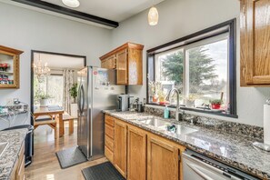 A modern kitchen with wooden cabinets, granite countertops, a stainless steel refrigerator, and a large window providing a view of the outdoors.