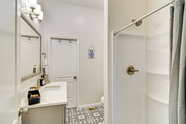 A bathroom with a white sink, mirror, and shower. There is a towel rack and a small sign on the wall. - Cumberland Lake Retreat: Furnished Deck & Grill! (Burnside)