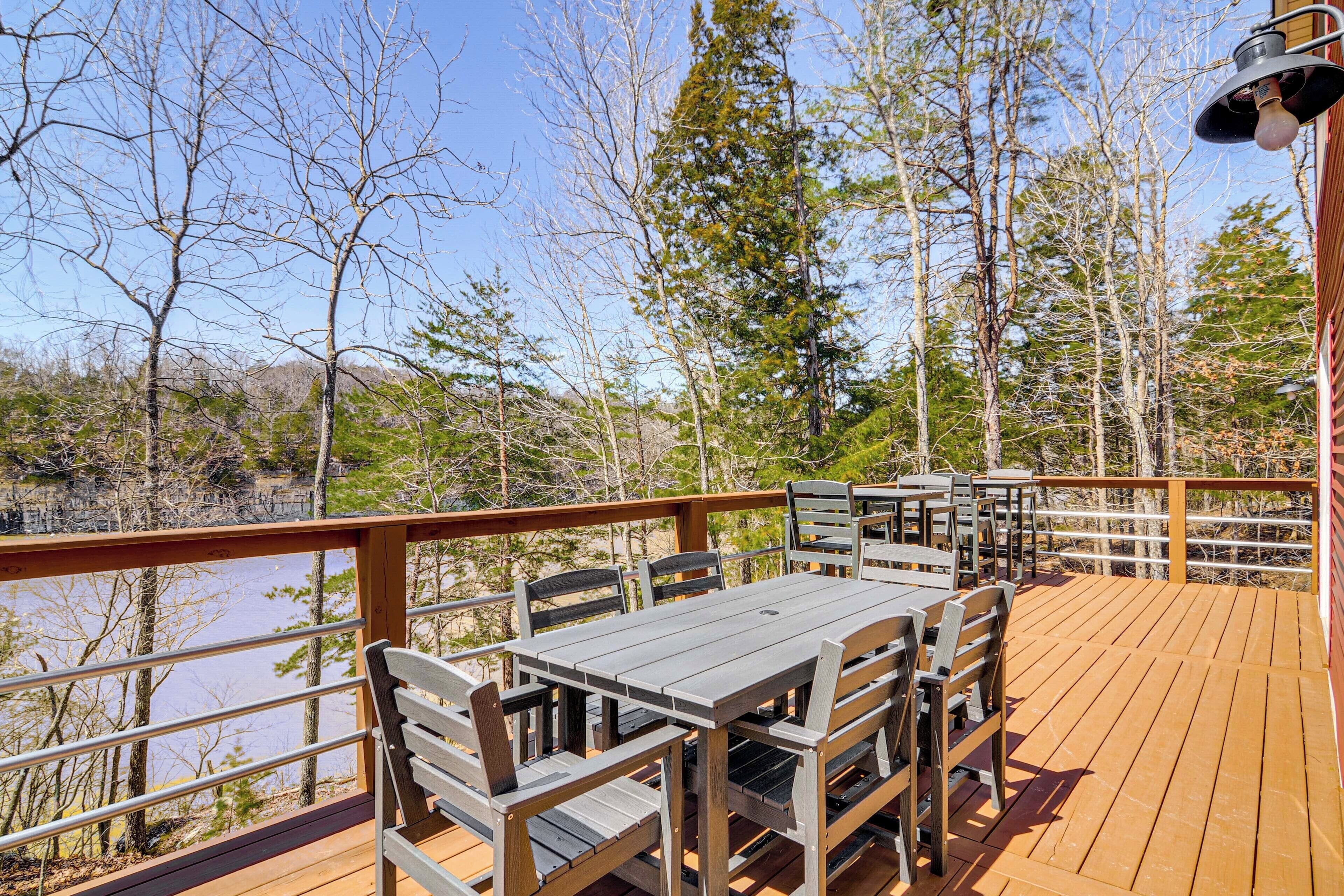 A wooden deck with a table and chairs overlooking a body of water and forested area.