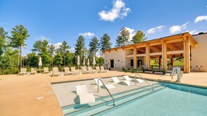 Ein Swimmingpool mit Liegestühlen und Sonnenschirmen, umgeben von Bäumen und einem überdachten Pavillon.