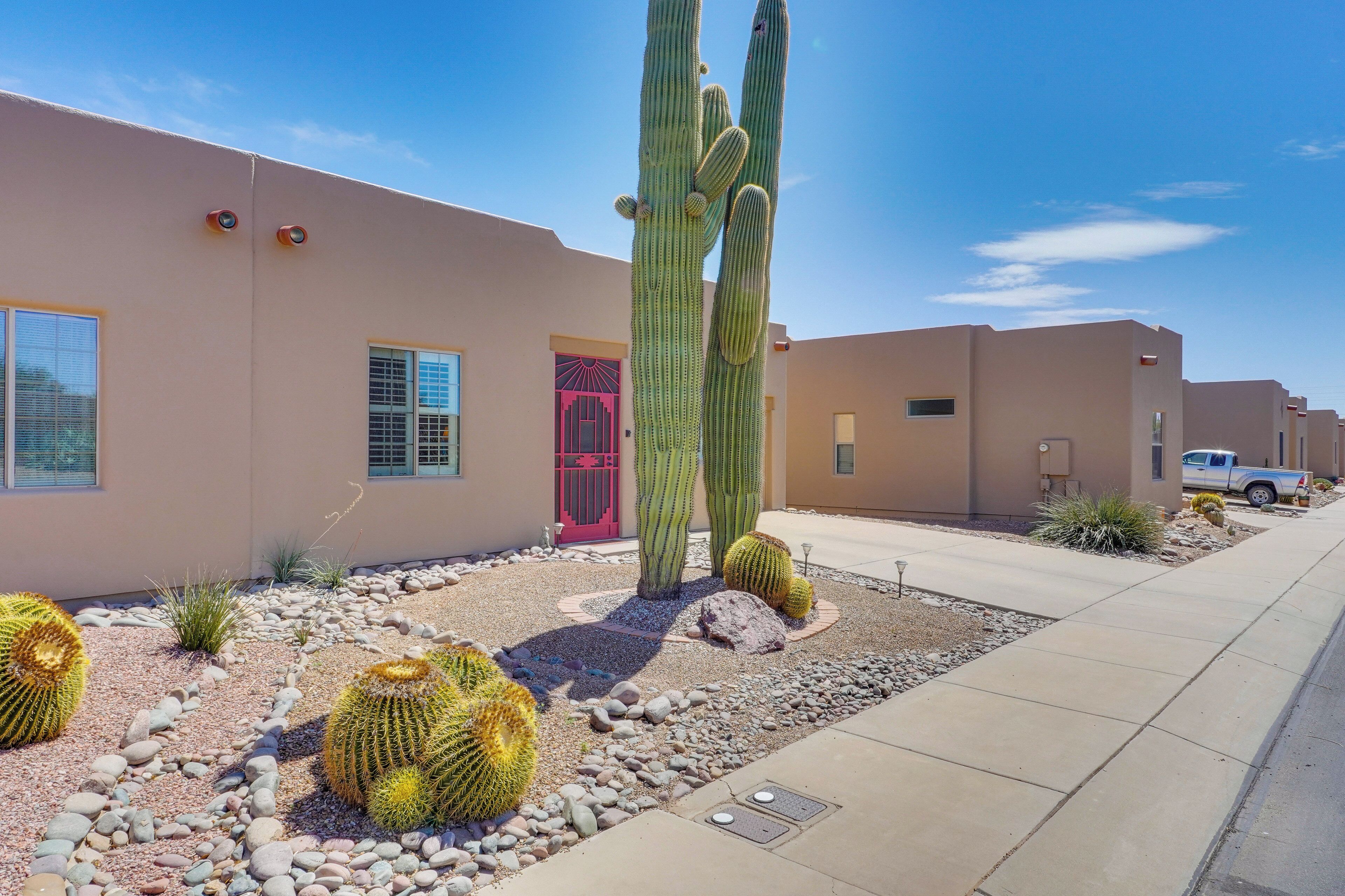Un edificio con un jardín desértico con cactus y una puerta roja.