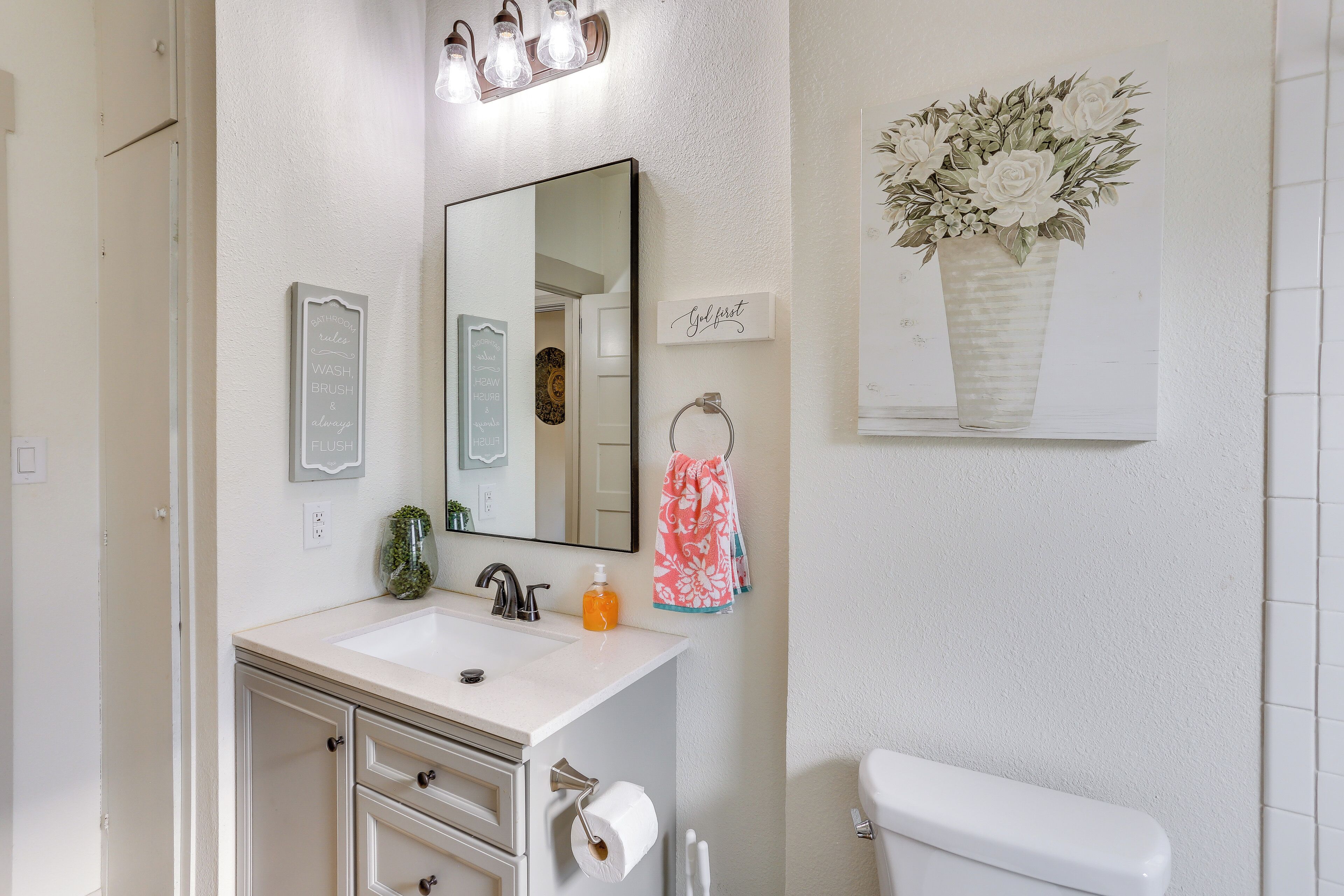 Un baño con un lavabo blanco, un espejo, un perchero para toallas, un inodoro y una obra de arte enmarcada en la pared.