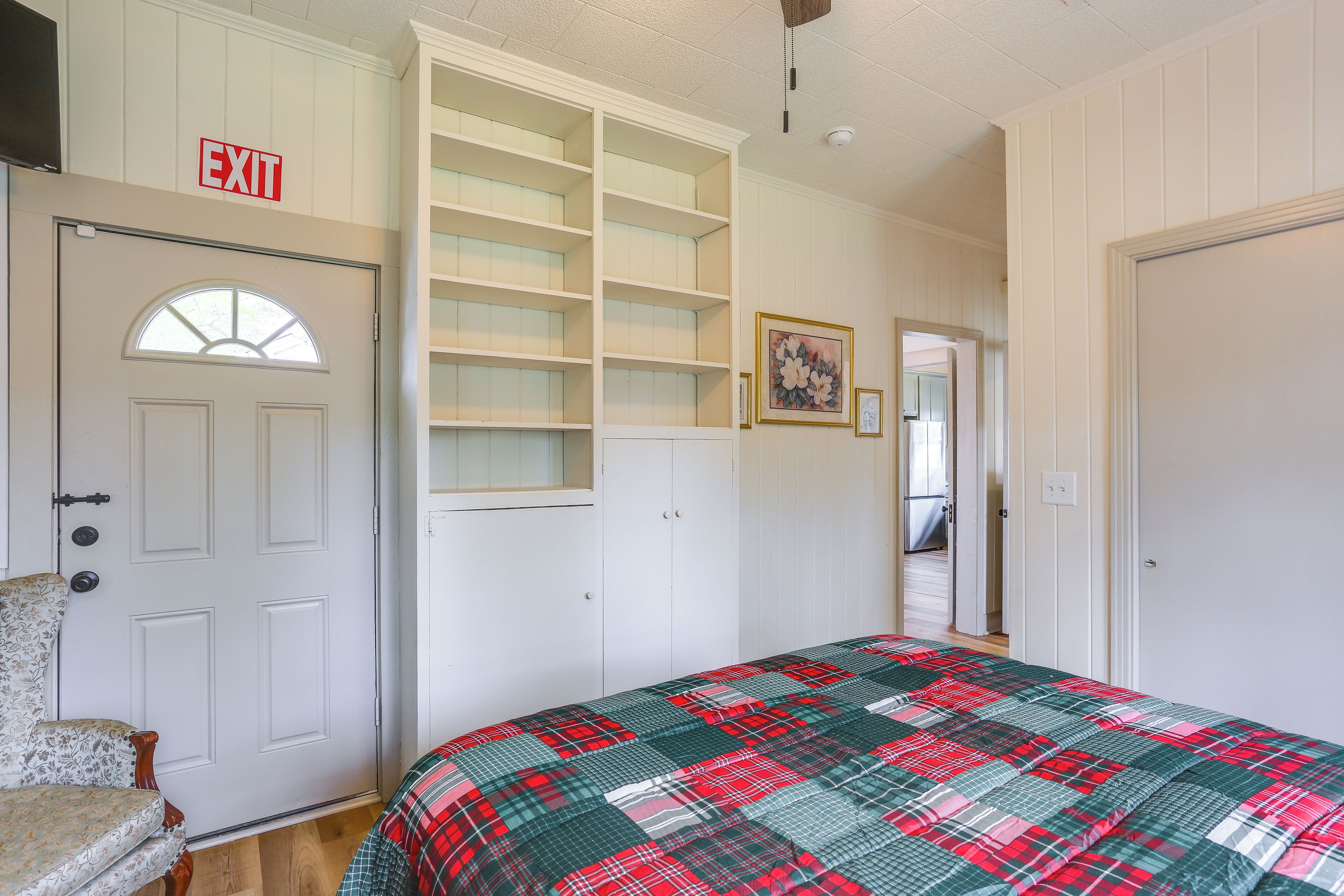 A bedroom with a bed, a chair, a wardrobe, and an exit sign.
