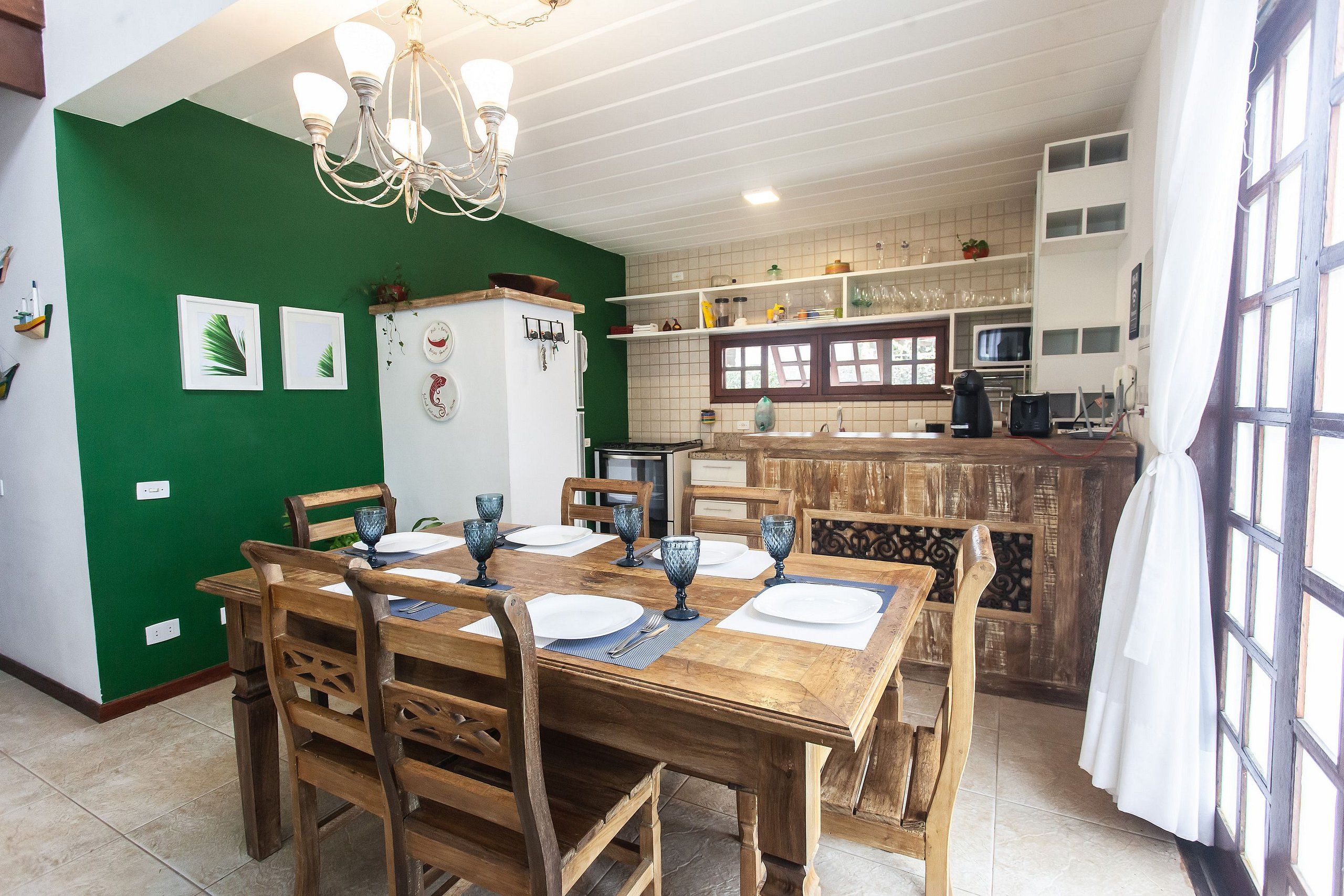 A dining area with a wooden table set for four, a refrigerator, and a kitchen in the background.
