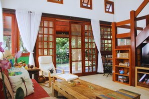 A spacious living room with a wooden coffee table, a comfortable chair, and a bookshelf. - Bz10 Casa 4 suítes em condomínio clube (Buzios)