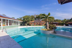 Ein Swimmingpool mit klarem, blauem Wasser, umgeben von Palmen und einem überdachten Bereich mit einem Kachel­dach.