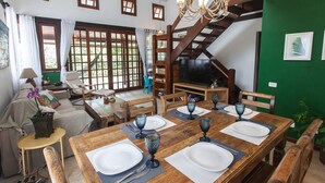 Un coin repas avec une table en bois dressée pour quatre personnes, un escalier et un téléviseur en arrière-plan.