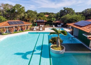 Een zwembad met betegeld zonnedek, omringd door ligbedden en een palmboom.