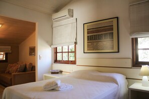 Hotelkamer met een bed, een raam met zonwering, een wandairconditioner, een ingelijst kunstwerk en een klein nachtkastje met lamp.