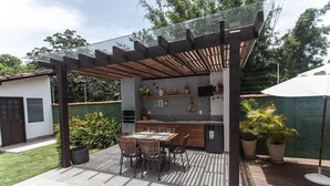 Un espace cuisine extérieur doté d’une pergola, d’une table à manger, de chaises et de plantes en pot.