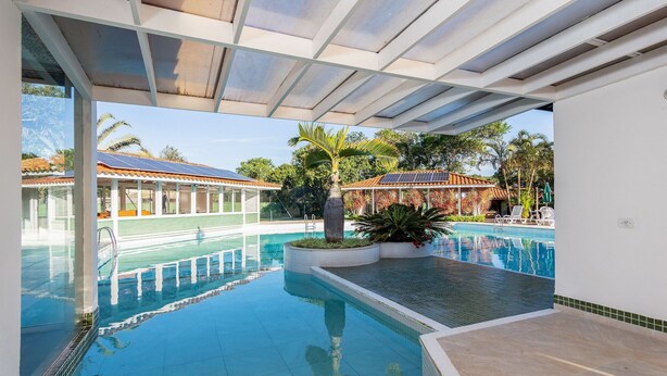 Une piscine à l’eau d’un bleu cristallin, entourée d’une zone abritée avec des poutres blanches et un sol carrelé.