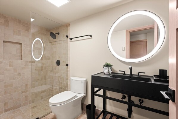A modern bathroom with a glass-enclosed shower, a white toilet, a black vanity with a mirror, and a small plant on the counter. - Timberline Lodge by Rove Hot Tub Patio w Views (Snowmass Village)