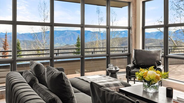 A modern living room with a large window overlooking mountains, a leather chair, and a coffee table with a vase of flowers. - Timberline Lodge by Rove Hot Tub Patio w Views (Snowmass Village)