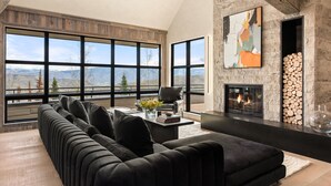 A modern living room with a large sectional sofa, a fireplace, and a view of mountains through large windows. - Timberline Lodge by Rove Hot Tub Patio w Views (Snowmass Village)