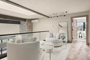 A modern living room with a large window, a round white sofa, a white armchair, and a small round table with a vase of flowers. - Timberline Lodge by Rove Hot Tub Patio w Views (Snowmass Village)