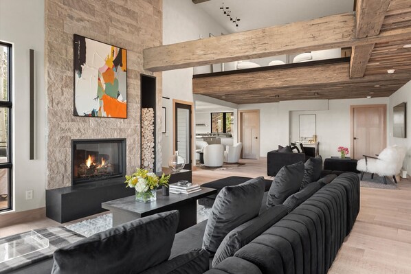 A modern living room with a fireplace, black sofas, and a large abstract painting. - Timberline Lodge by Rove Hot Tub Patio w Views (Snowmass Village)
