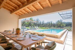Comedor con vista a la piscina, techo de madera y mobiliario exterior.