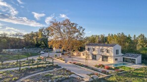 Una casa moderna con piscina, rodeada de jardines ajardinados y árboles.