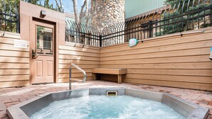 A hot tub in a wooden outdoor area with a stone wall and a metal fence. - Top Floor and Spacious, One block to Everything! (Breckenridge)