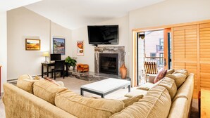 A living room with a sofa, a coffee table, a fireplace, a TV, and a dining area. - Top Floor and Spacious, One block to Everything! (Breckenridge)