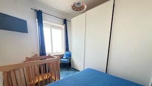 A bedroom with a wooden crib, a blue bed, a chair with a blue cushion, and a window with curtains. - Cataldo guest house Capri center (Marina Grande)