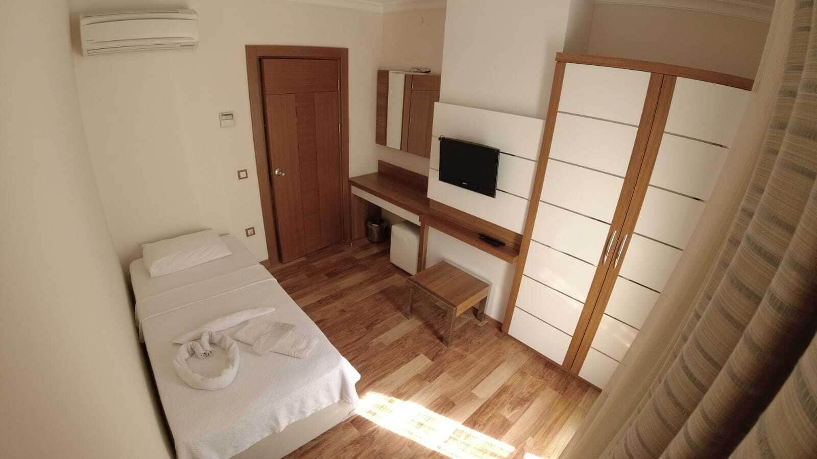 A bedroom with a bed, a TV, a wardrobe, and a small desk.