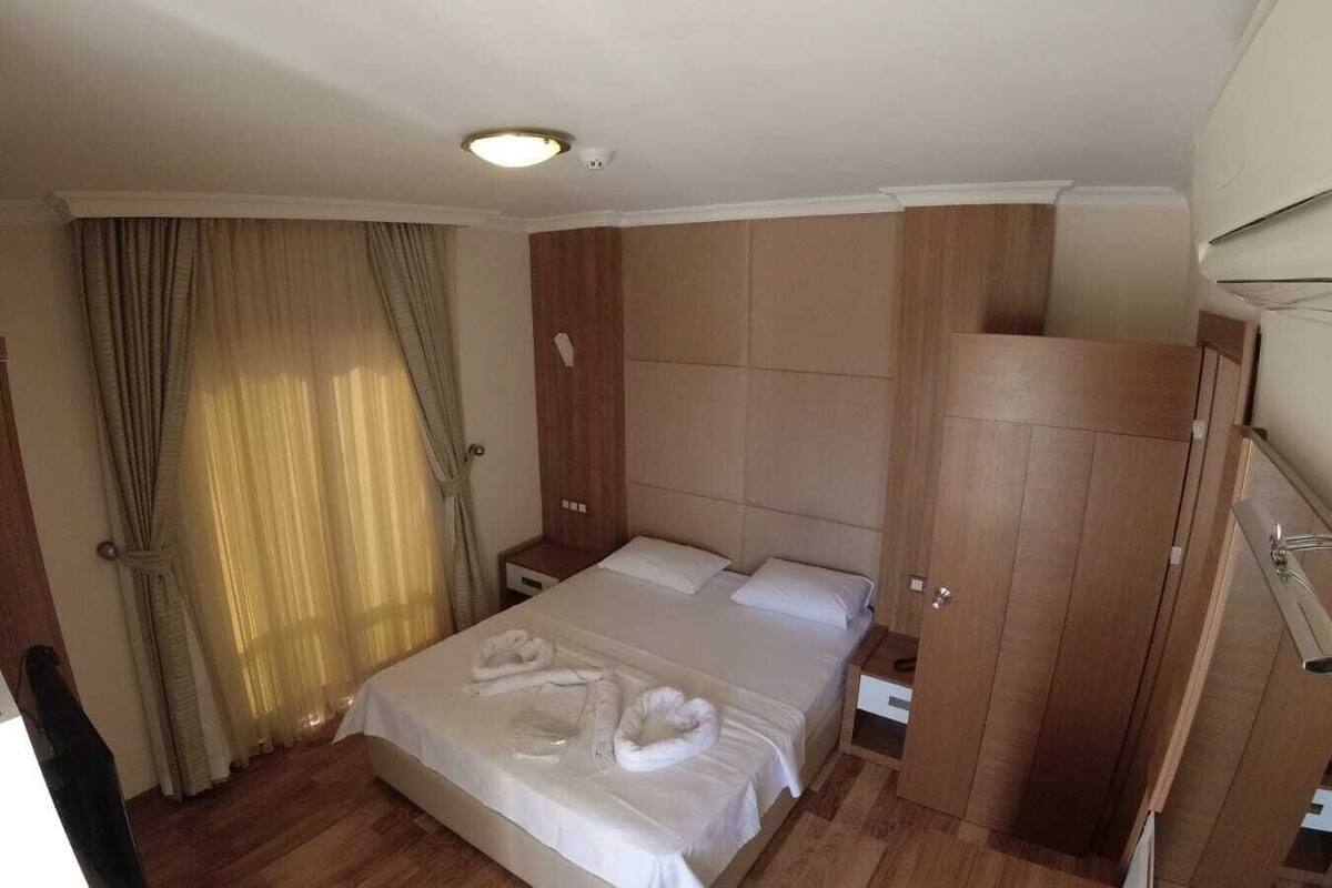 A hotel room with a bed, wooden wardrobe, and a nightstand.