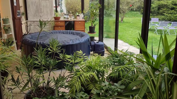 Een oranjerie met een jacuzzi, omringd door weelderige planten en uitzicht op een tuin.