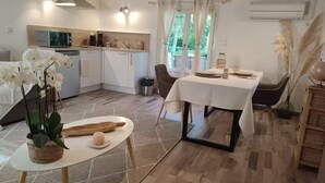Een moderne keuken met witte kasten, een magnetron en een koffiezetapparaat. Er is een eethoek met een tafel gedekt voor twee personen, een vloerkleed en een plant.