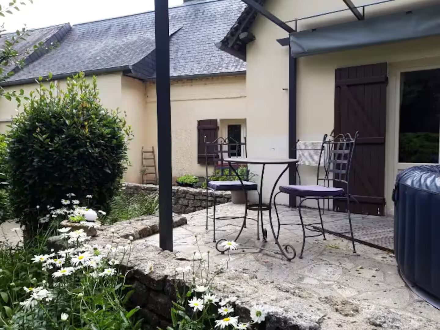 En terrasse med et bord og stole, et spabad, og en have med blomster.