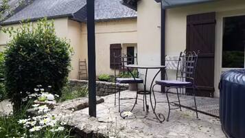 En terrasse med et bord og stole, et spabad, og en have med blomster.