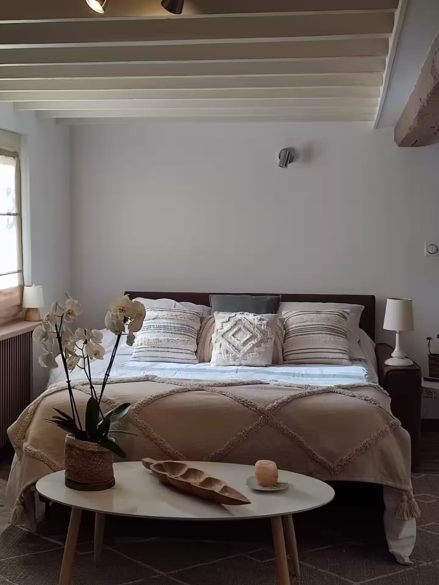 A bedroom with a bed, bedside tables, a small round table, and a potted plant.