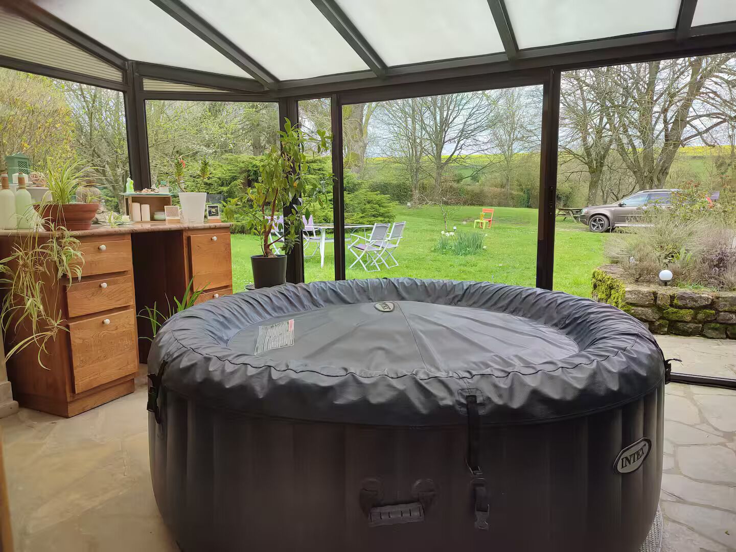 A hot tub in a covered outdoor area with a view of a grassy yard and a car in the background.