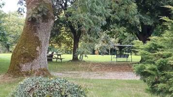 A park with a picnic table, a swing set, and a large tree.