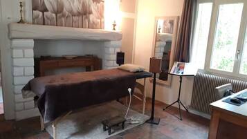 A room with a bed, a small table, a chair, a radiator, and a window with curtains.