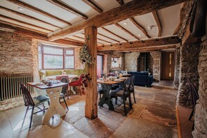 A rustic interior with exposed wooden beams, stone walls, and a dining area with a table and chairs.