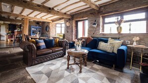 A spacious living room with exposed wooden beams, a brown leather sofa, a blue sofa, and a round wooden coffee table. - Hanley House (Tenbury Wells)